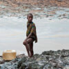 A boy with a fishing net stands on the crude oil-stained bank of a rift in the creek area in Niger Delta.
